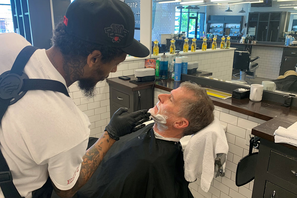 Barber applying shaving cream to a reclining client’s face